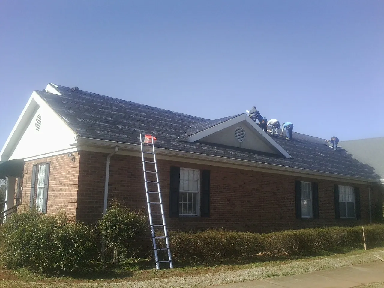 Crew tearing shingles off a brick ranch roof with a ladder set — Emergency Roof Repair work by our crew in Gallipolis