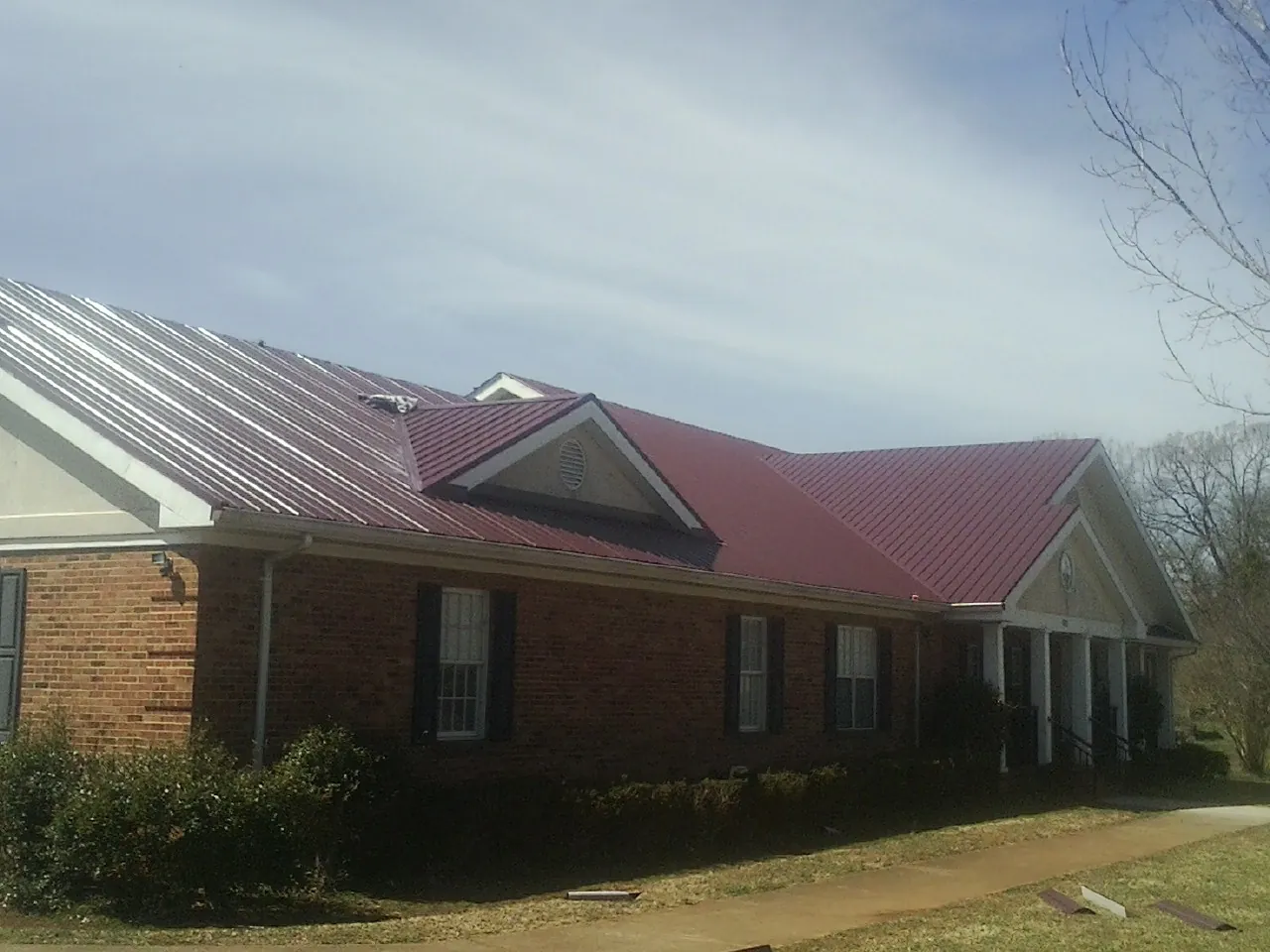 Red metal roof with gabled entries on a long brick building, from a Hail Damage Roof Repair job in Gallipolis