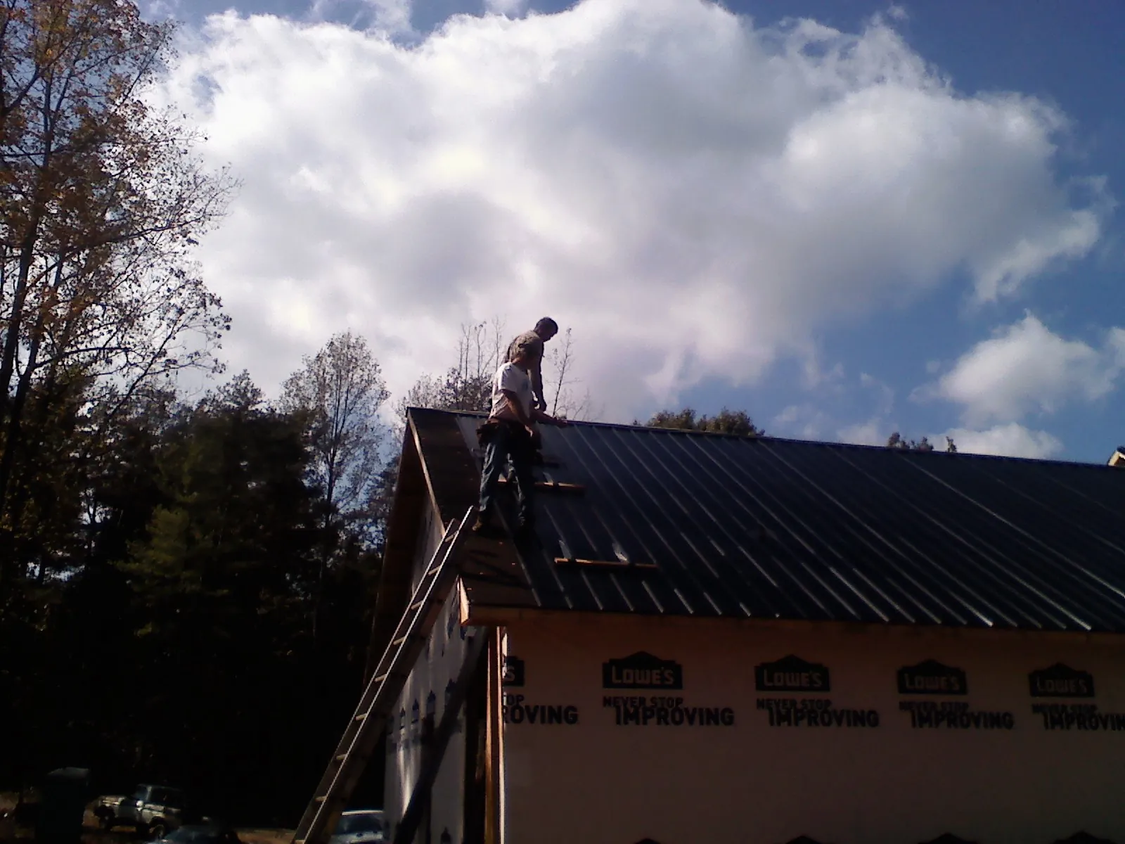 Roofer fastening dark metal panels high against a cloudy sky, from a Roof Inspection job in Gallipolis